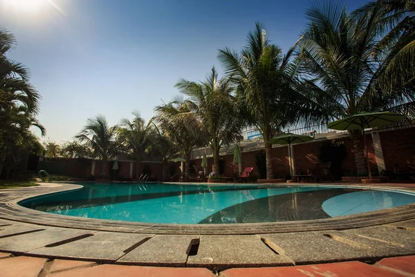 swimming pool with blue water surrounded by brick fence palms and sun umbrellas on hotel territory