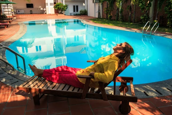 tatlı kız sarı bluz ve kırmızı pantolon otel Yüzme Havuzu, şezlong palms tarafından dayanmaktadır