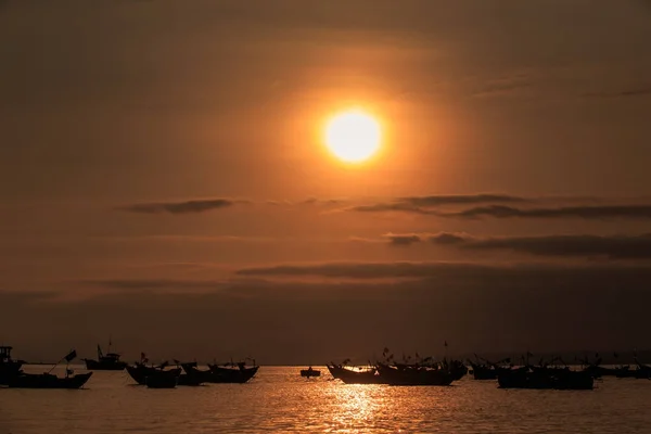 大橙色太阳盘在云彩之中在黑暗的天空在海洋与渔船剪影在日落 — 图库照片