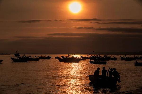 大橙色太阳盘在云彩之间在黑暗的天空在宁静的海洋海湾之上与小船和人剪影在日落 — 图库照片