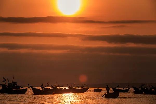 amazing view fishing boat silhouettes in calm ocean bay and large orange sun disk above clouds in dark sky at sunset