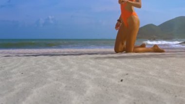 çekici sarışın genç kadın turuncu mayo altın bitcoin gerçek modelleri plaj kum gizler.