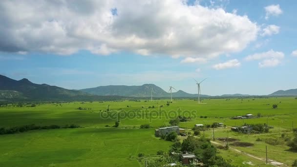 慢飞行在宽广的绿色领域之上与现代清楚的风发电站和山在背景 — 图库视频影像