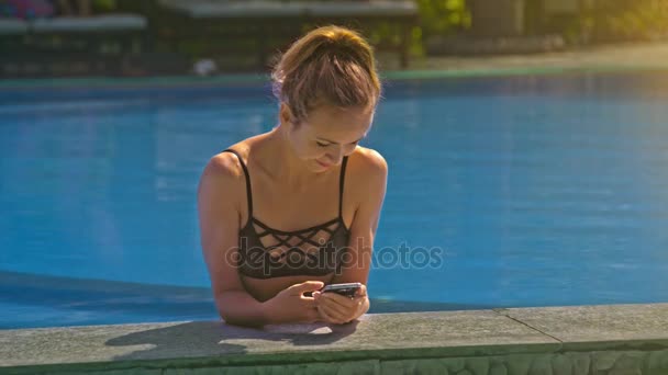 漂亮苗条的金发碧眼的女孩通过现代智能手机 Waterpool 在温暖的阳光明媚的日子里 — 图库视频影像