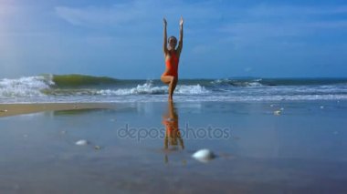 Genç sarışın kız standları Yoga resimsel okyanus dalgaları karşı ıslak plaj kum kenarında Virabhadrasana poz