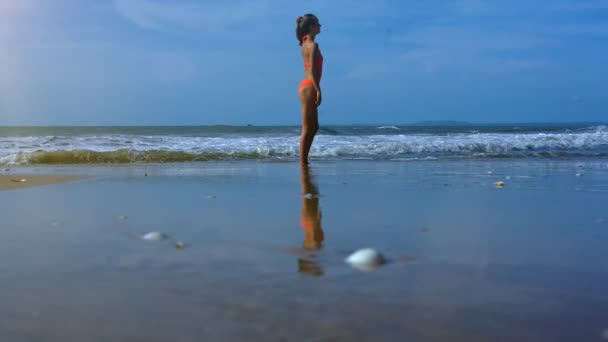 侧面视图苗条的女孩在橙色泳装舒展前做瑜伽在海滨附近海浪冲浪 — 图库视频影像
