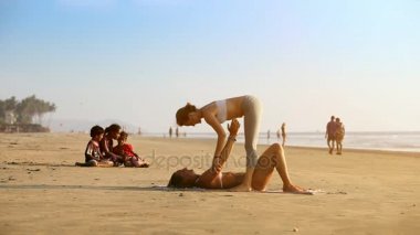 Goa, Hindistan - 09 Aralık 2012: Çift yoga kız yalanlar üzerine geri tutan diğer kız vücut gergin kolu tarafından deniz üzerinde 09 Aralık Goa içinde yapıyor Hintli çocuk watch Avrupa Kadınlar