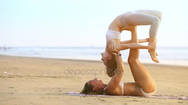 白ビキニの女の子がヨガ ゴアで静かな紺碧の海に対して 日ポーズ橋で伸ばされた足で金髪のパートナーを保持をカップルはゴア インド 2012 — ストック動画