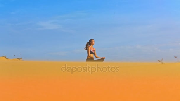 黄金の砂と無限の青空間ヨガ蓮華座に座っている素晴らしいビュー金髪長い髪の女の子 — ストック動画