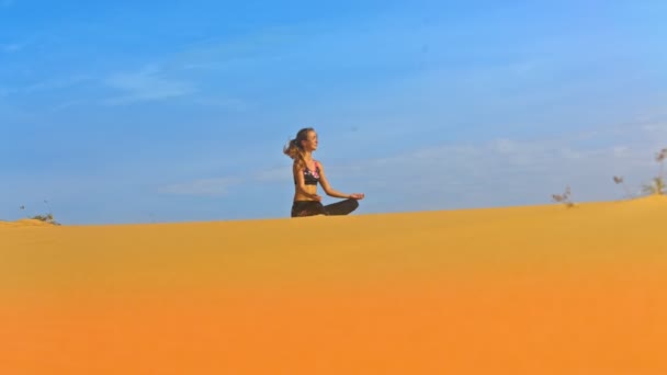 青い空を背景に金色の砂に瞑想のポーズで座っている美しい少女の下から素晴らしい景色 — ストック動画