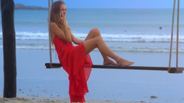Langhaariges Mädchen Rotem Sarafan Schaukelt Mit Handy Barfuß Auf Strandbank — Stockvideo