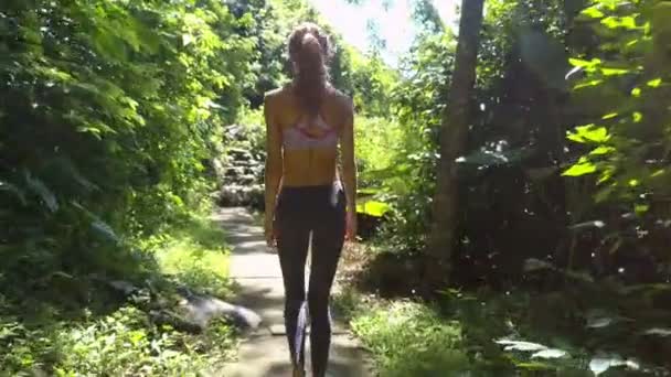 背面视图苗条的运动金发女郎走在热带绿色植物之间的石轨道到古楼梯 — 图库视频影像