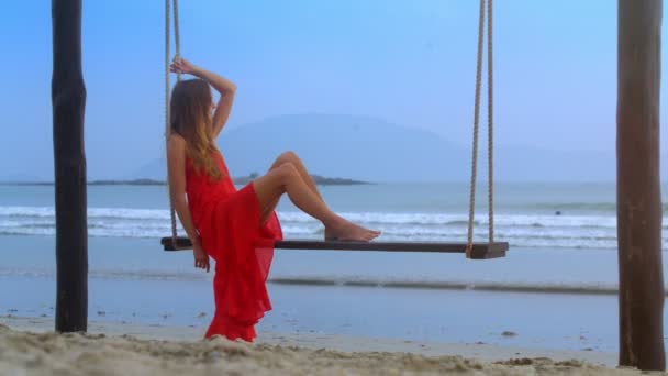 Rückansicht Blondes Langhaariges Mädchen Barfuß Rotem Kittel Schaukelt Auf Strandseilbank — Stockvideo