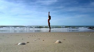 yan görünümü atletik kız parlak mayo wavesurf karşı ıslak kum üzerinde değişen pozisyonlar yoga yapar