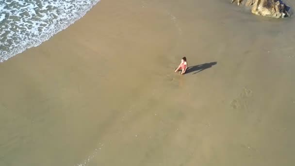 vue aérienne femme en maillot de bain rouge change de pose de yoga sur la plage couverte de pierres contre la mer paisible 