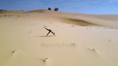 yoga konumda açık gökyüzü karşı geniş çöl kumları arasında kız uzun at kuyruğu ayakta yüksek hava görünümünü Rüzgar sallıyor
