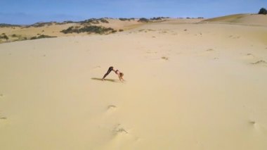 Panorama güçlü ince kız siyah arka planda çöl kum ve açık gökyüzü arasında zor yoga egzersizleri yapıyor