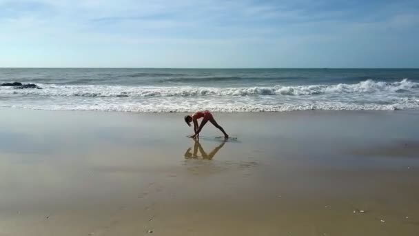 鸟瞰蔚蓝的海浪在湿沙上翻滚女孩在蓝天下的沙滩上改变体育锻炼 — 图库视频影像