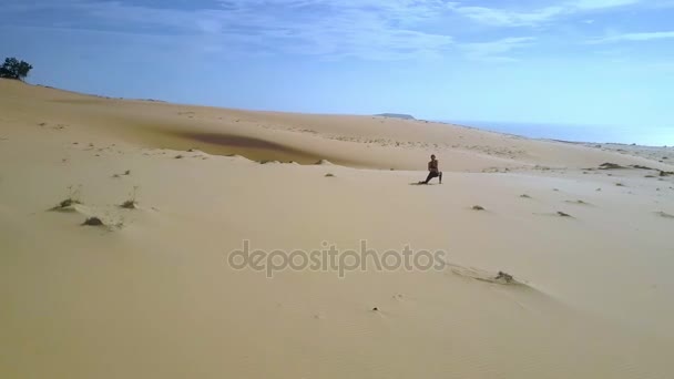 vue aérienne approchant mince fille faisant des positions de yoga sur de vastes sables du désert contre fantastique ciel bleu profond sans fin 
