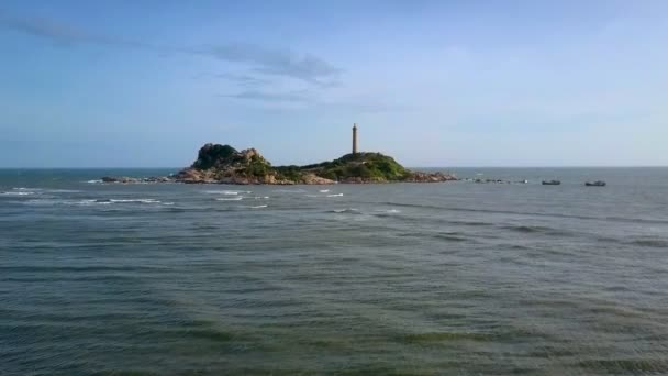 幻想的な紺碧の海の泡波を海岸と空に対して歴史的な灯台と岩だらけの島の間にローリングで移動します — ストック動画