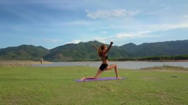 Flycam Gölü kıyısında başının üstünde el ile yoga egzersiz yapıyor sarışın ince kadın taşır