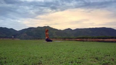 Flycam kaldırır yoga oturan adil saçlı kızdan uzak tepelik orman karşı göl kıyısında Vajrasana poz