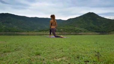 Flycam side görünümü güzel kız tutan yoga poz resimsel göl ve muhteşem tepeler karşı