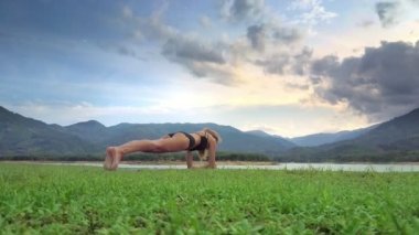 yan görünümü genç ince sarışın kız yoga pozisyon bükülmüş kollar ve göl dağlık manzara karşı ayaklarına yatan tutar