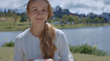 uzun at kuyruğu ile portre sevimli genç kız gülümsüyor içecek çay Kupası karşı nehir manzara Cafe'de etrafında görünüyor