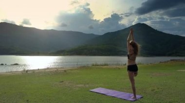 Flycam görünümü uzun boylu kız standları Yoga barışçı nehir güneş ışınları altında parlayan karşı Vrikshasana poz