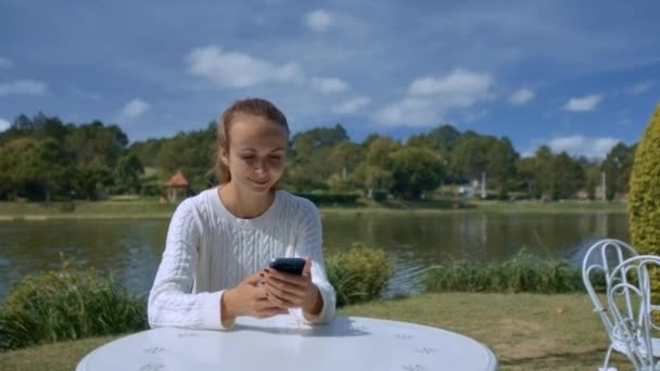 Bela Menina Loira Suéter Branco Envia Smartphone Sms Mesa Restaurante — Vídeo de Stock