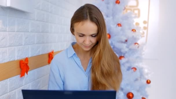 美丽的年轻女孩与松散的流动头发工作的计算机在灯光室与设计师白圣诞树 — 图库视频影像