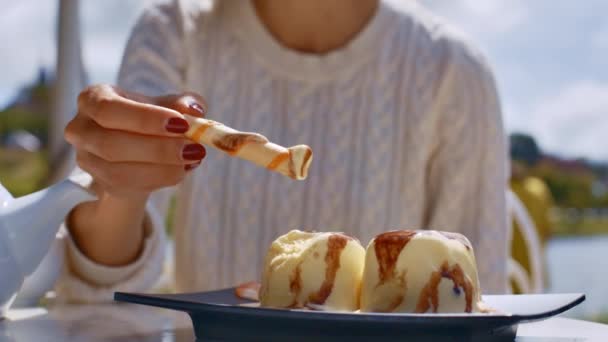 特写女人在白色毛衣在阳光明媚的日子在餐馆吃可口的冰淇淋与甜管 — 图库视频影像