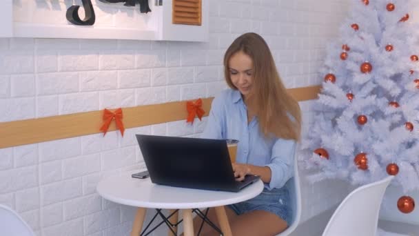 金发女孩在笔记本电脑上工作在白色人造圣诞树与红色球在光室 — 图库视频影像