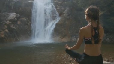 tatlı kız uzun bezleri ve çıplak geri yoga poz şelale orman arasında çalışan tarafından rahatlatır.