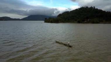 Beyaz tişörtlü adam Panorama pirogue Gölü küçük köy ve uzak yeşil tepeler karşı yola çıkacak