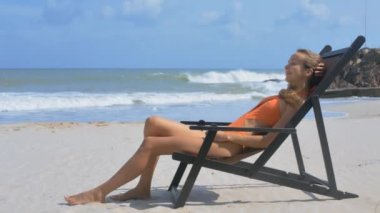 ahşap şezlong kum okyanus plaj yan görünümü sarı uzun saçlı kız turuncu mayo rahatlatır