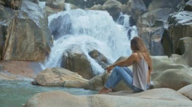 yan görünümü güzel sarışın çıplak ayakla kız kot pantolon oturur ve şelale art arda sıralı buzlu görünüyor