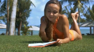 tatlı kız bikini çim plaj düzgünleştirir uzun saç Rüzgar tarafından sallayarak kağıt kitap okyanus karşı yazıyor üstünde tans