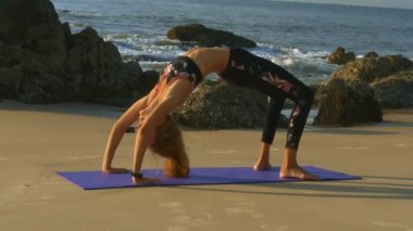 güzel mutlu kız oturur ve mat boş plaj ve arka planda gökyüzü arasında fitness egzersizleri yapıyor