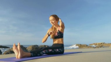 güzel mutlu kız oturur ve mat boş plaj ve arka planda gökyüzü arasında fitness egzersizleri yapıyor