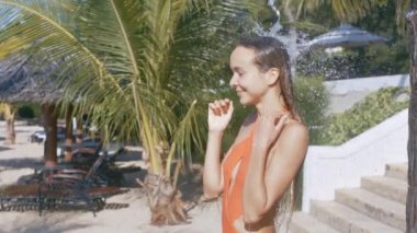 yan görünümü çekici uzun saçlı kız turuncu bikini plaj taş merdiven ve palmiye ağaçları karşı duş alır