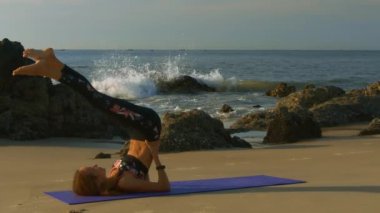 Ince sarışın kız siyah tayt ve en iyi uygulamaları yoga karşı dalgalar ve berrak gökyüzü masmavi okyanus plaj üzerinde poz veriyor
