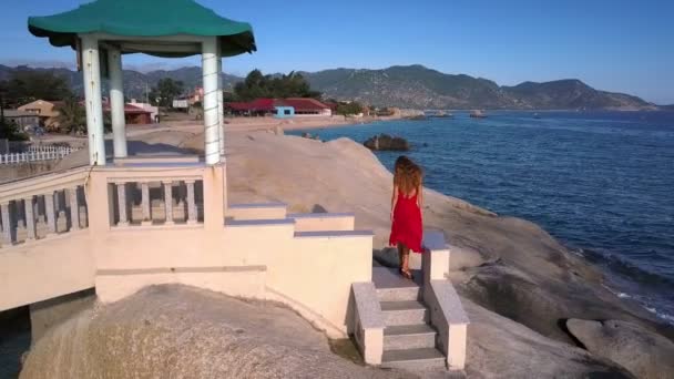 wunderbare Luftaufnahme Blondes Mädchen in rotem Kleid vom Wind gewunken Spaziergänge entlang Steinbrücke über dem Ozean