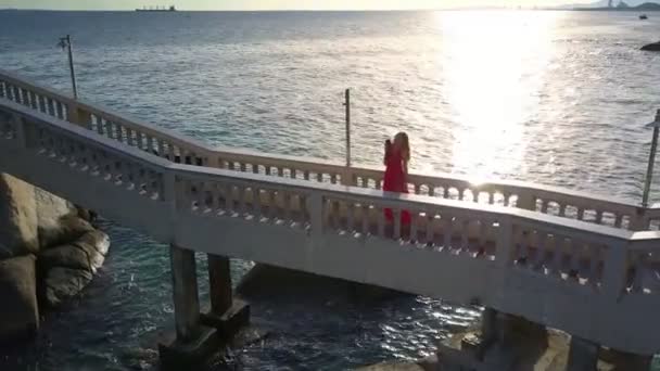 空中パノラマ赤色 Selfie 海の水に太陽光の反射に対して石の橋の上で金髪女性 — ストック動画