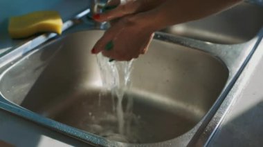 Kız eller kırmızı manikür ile toz bezi üzerinde çelik mavi duvarlı modern mutfak lavaboda su akışı altında sıkmak