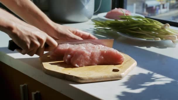 クローズ アップの女の子が板上にキッチンの窓際でネギ束近く美味しい料理の大規模なカット肉部分を準備します — ストック動画