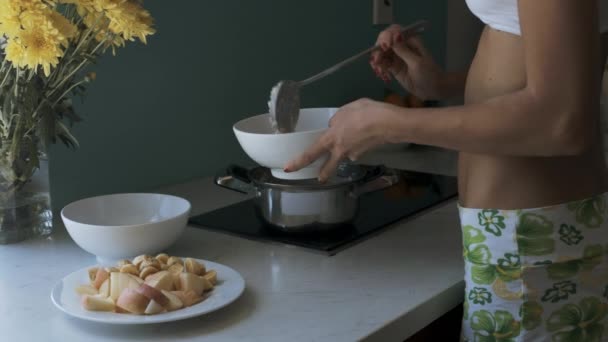 クローズ アップ女性は黄色の花で飾られたキッチンの白いボウルに鍋から熱いお粥を置く — ストック動画