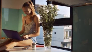 güzel sarışın Bayan krizantem cam vazo içinde sunulan yakınındaki geniş pencere üzerinde oturan at kuyruğu ile laptop ve rüyalar kapatır