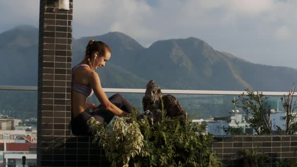 美丽的女人摘下耳机放在屋顶阳台上的书籍反对摄影胜地城市 — 图库视频影像